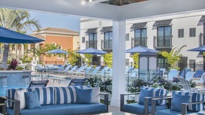A rooftop lounge area with blue-striped sofas and tables, a pool with sun loungers, and umbrellas. - Inn on Fifth (Naples)