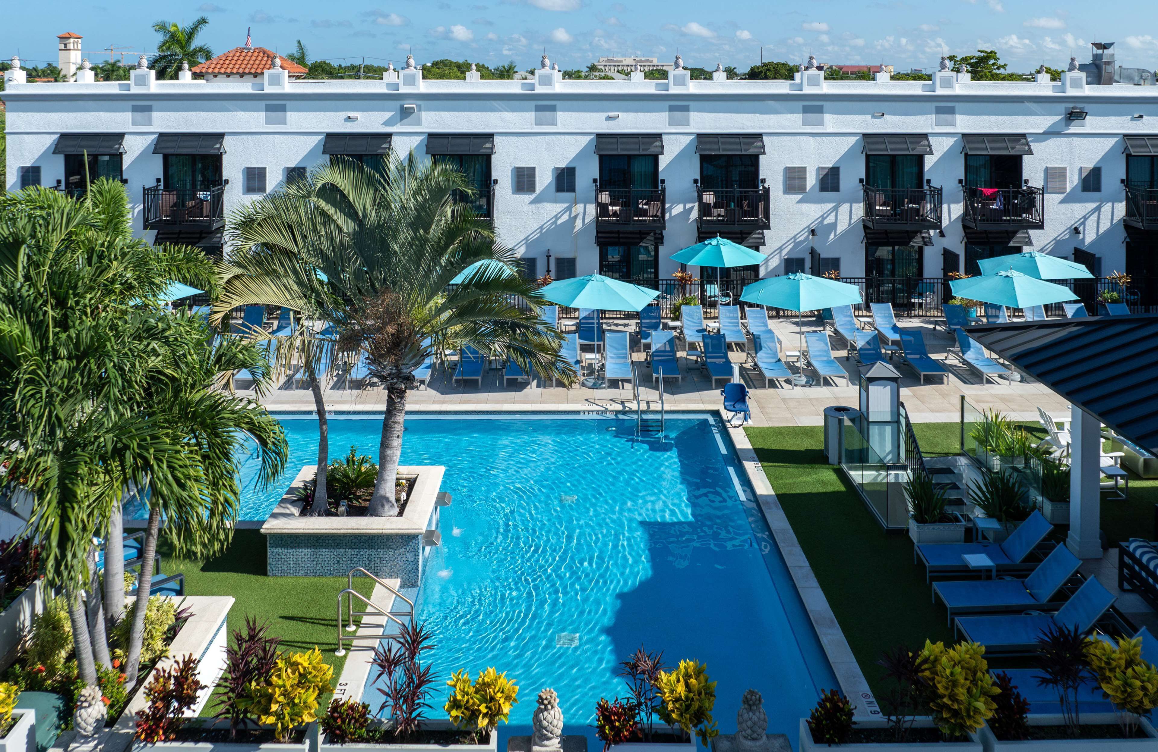 A pool area with lounge chairs and umbrellas, surrounded by a white building with balconies.