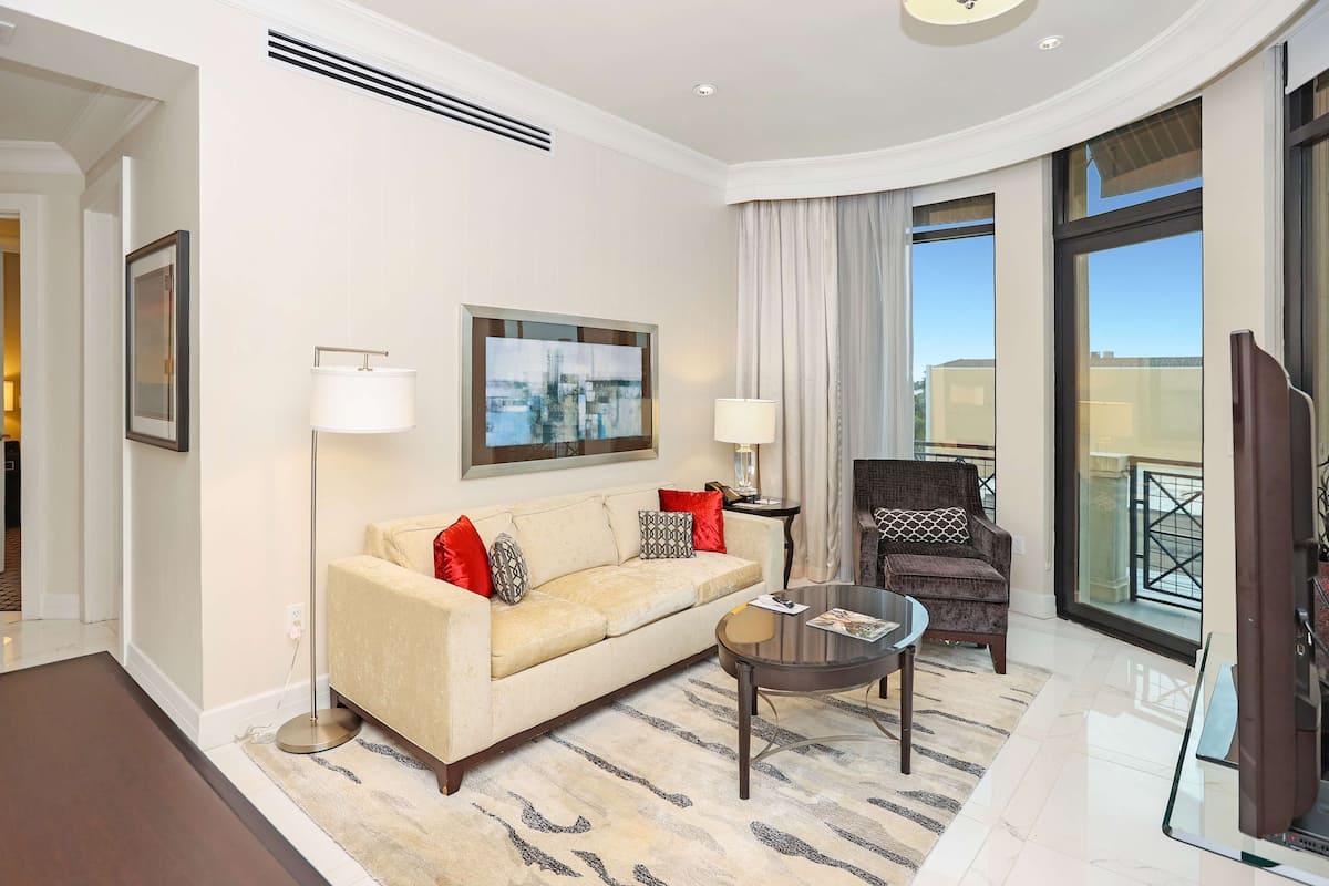 A modern hotel room with a sofa, armchair, and a glass coffee table.