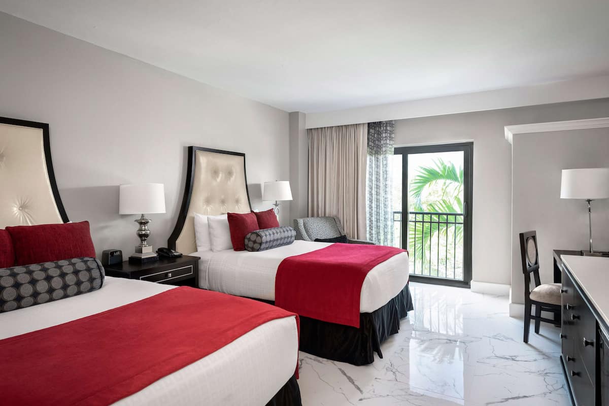 A hotel room with two beds, a desk, and a view of the outdoors.