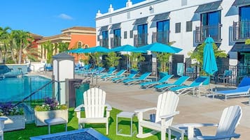 Un espace piscine d’hôtel avec des chaises longues, un jacuzzi et un bâtiment doté de balcons.