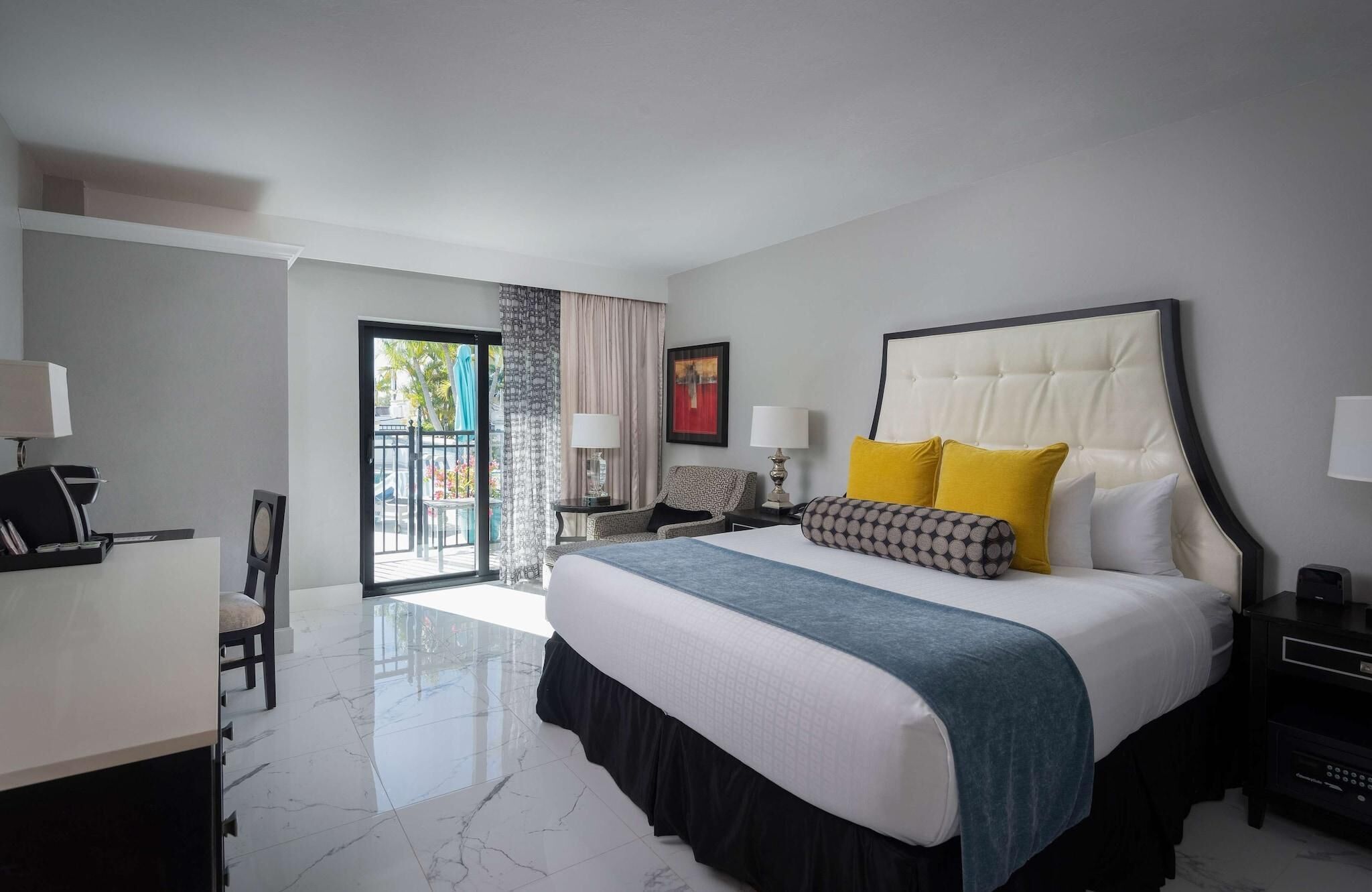 Une chambre d’hôtel comprenant un lit, un bureau, une chaise, une table de chevet, une lampe, un tableau et une vue sur l’extérieur, accessible par une porte coulissante.