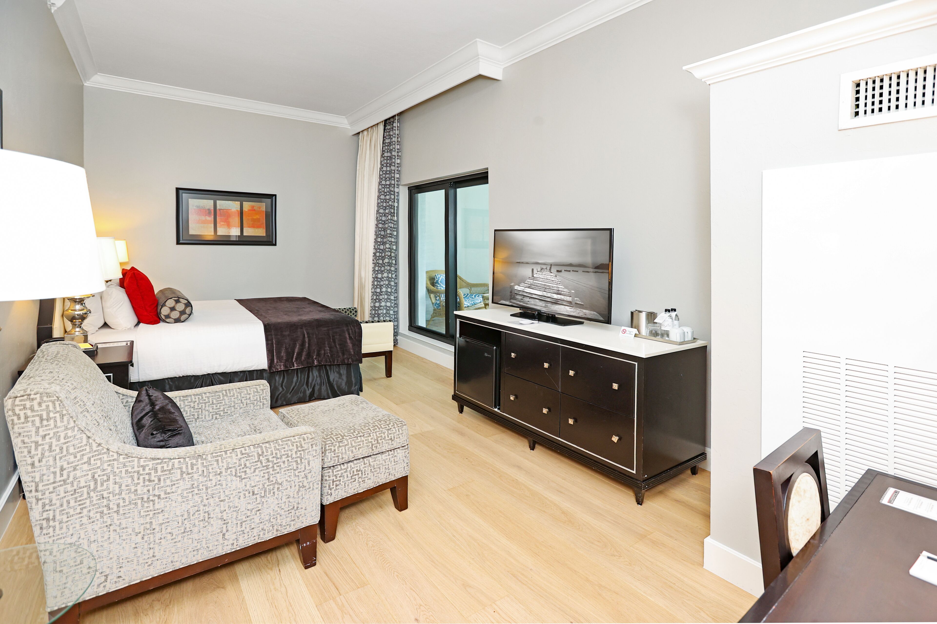 A hotel room with a bed, a sofa, a TV, a desk, and a window.