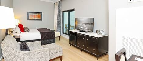 A hotel room with a bed, a sofa, a TV, a desk, and a window.