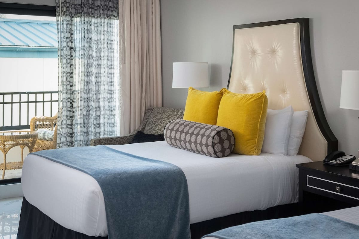 A hotel room with a large bed, two bedside lamps, a nightstand with a phone, and a view of the outside balcony.