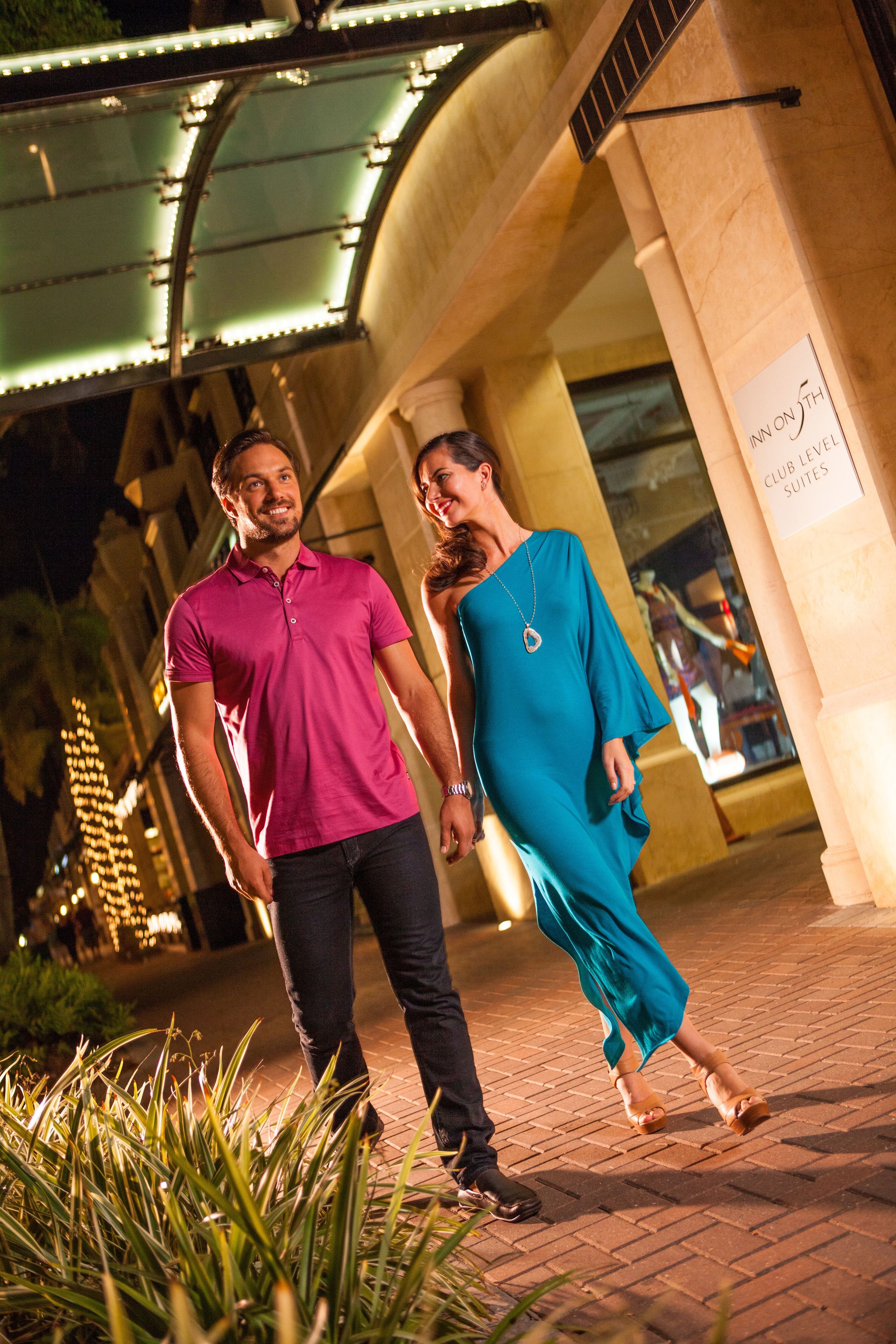 A couple walking on a paved pathway with a building in the background.