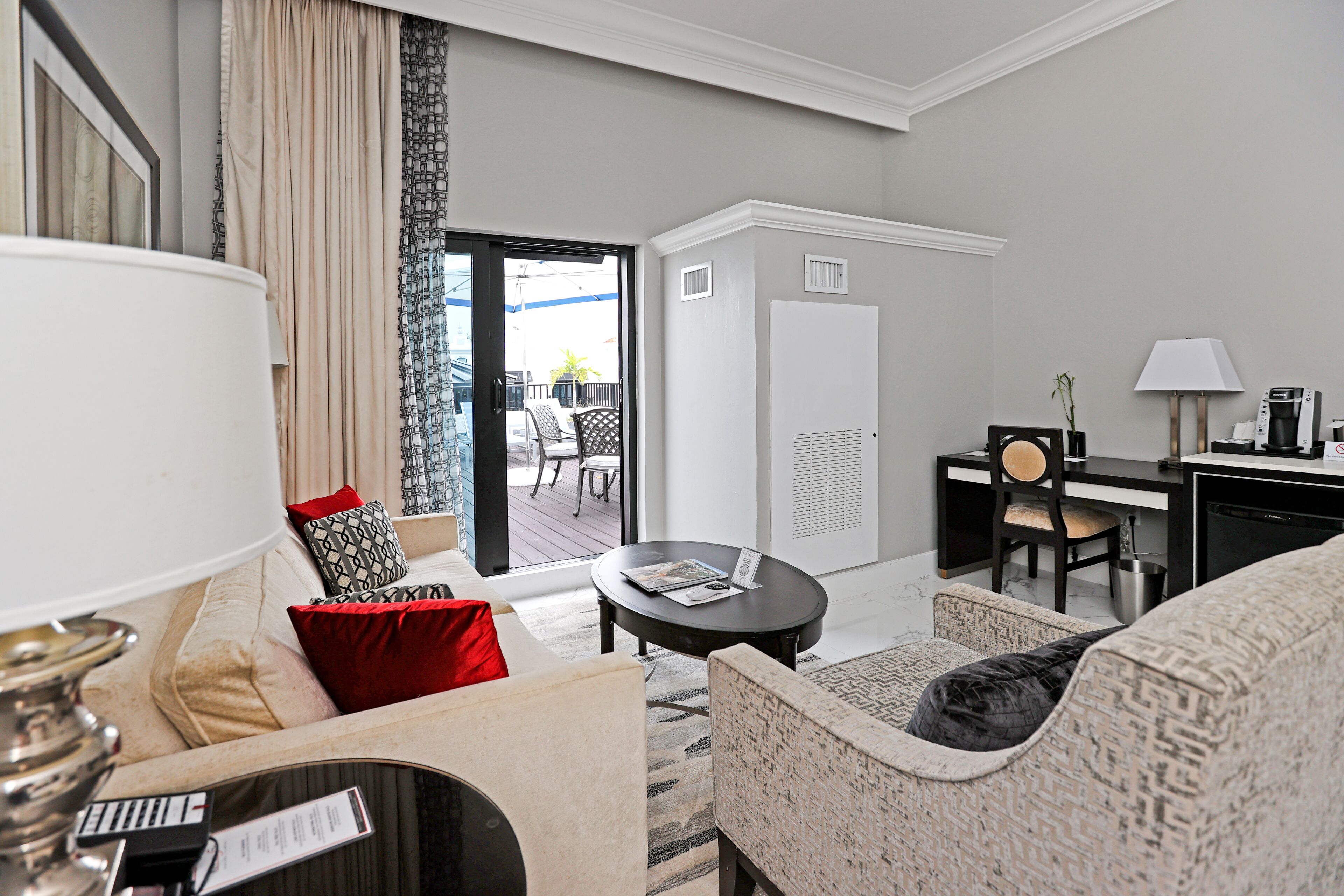 Ein modernes Hotelzimmer mit Sofa, Sessel, Couchtisch, Schreibtisch und Blick auf den Balkon.