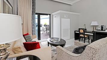 Ein modernes Hotelzimmer mit Sofa, Sessel, Couchtisch, Schreibtisch und Blick auf den Balkon.