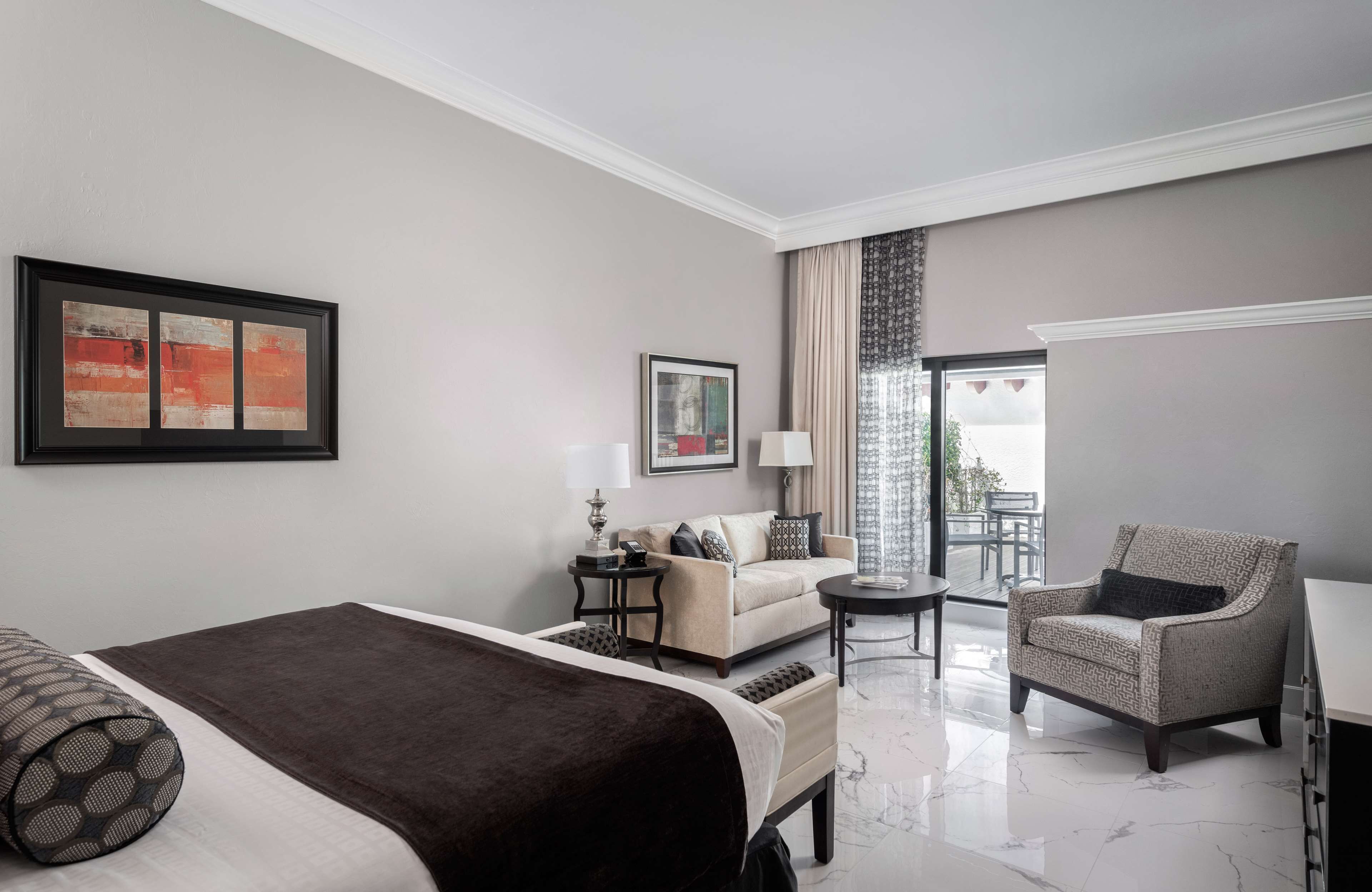Quarto de hotel com cama, sofá, cadeira, mesinha e varanda com vista.