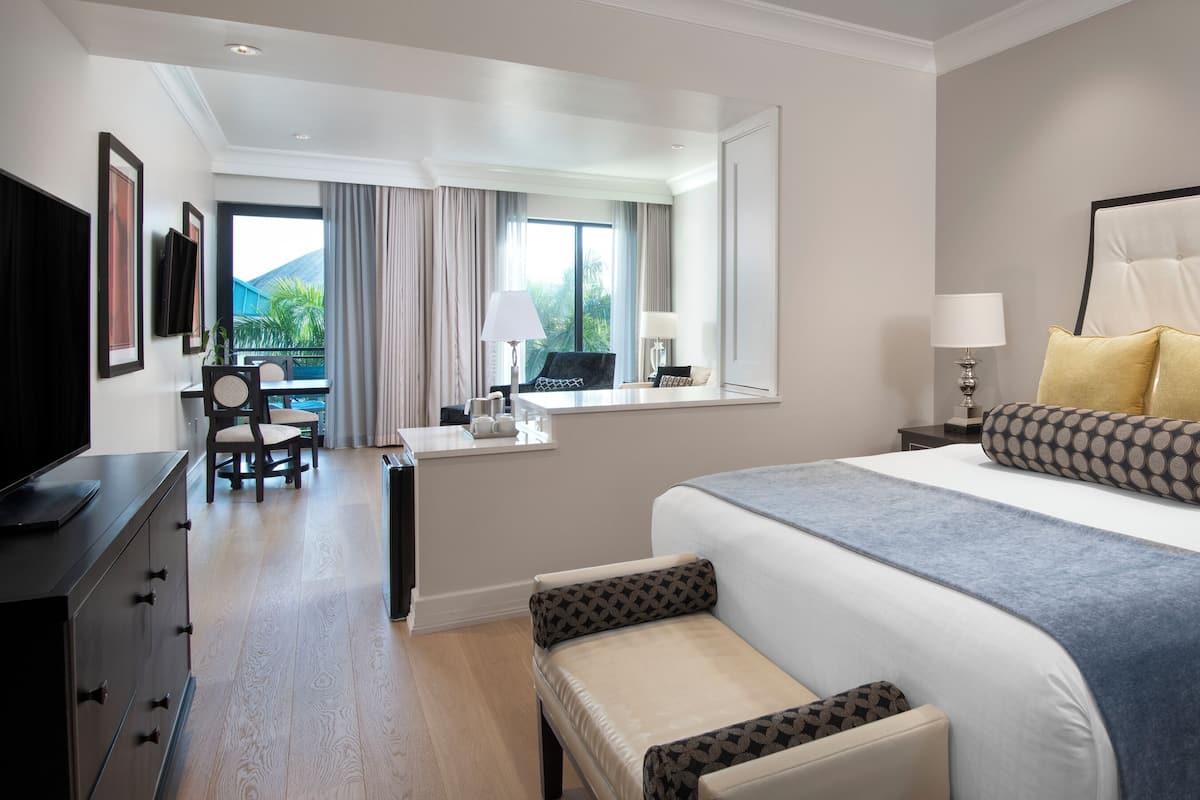 A hotel room with a large bed, a desk, a chair, and a view of the outdoors.