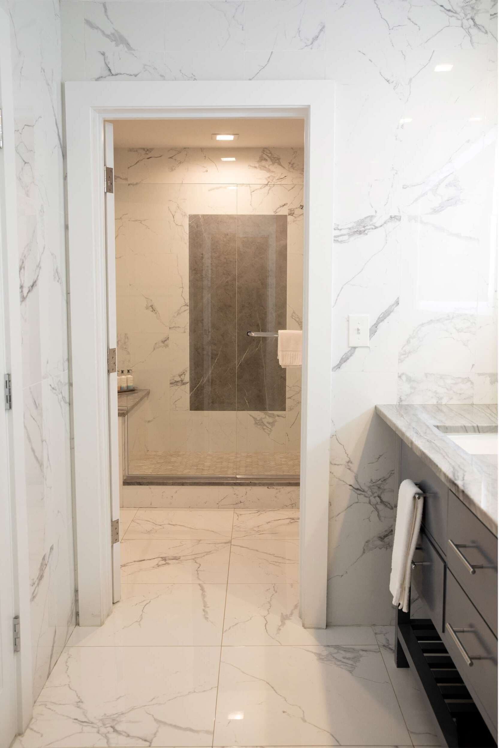 A modern bathroom with marble walls and floor, a glass shower enclosure, and a dark marble sink.