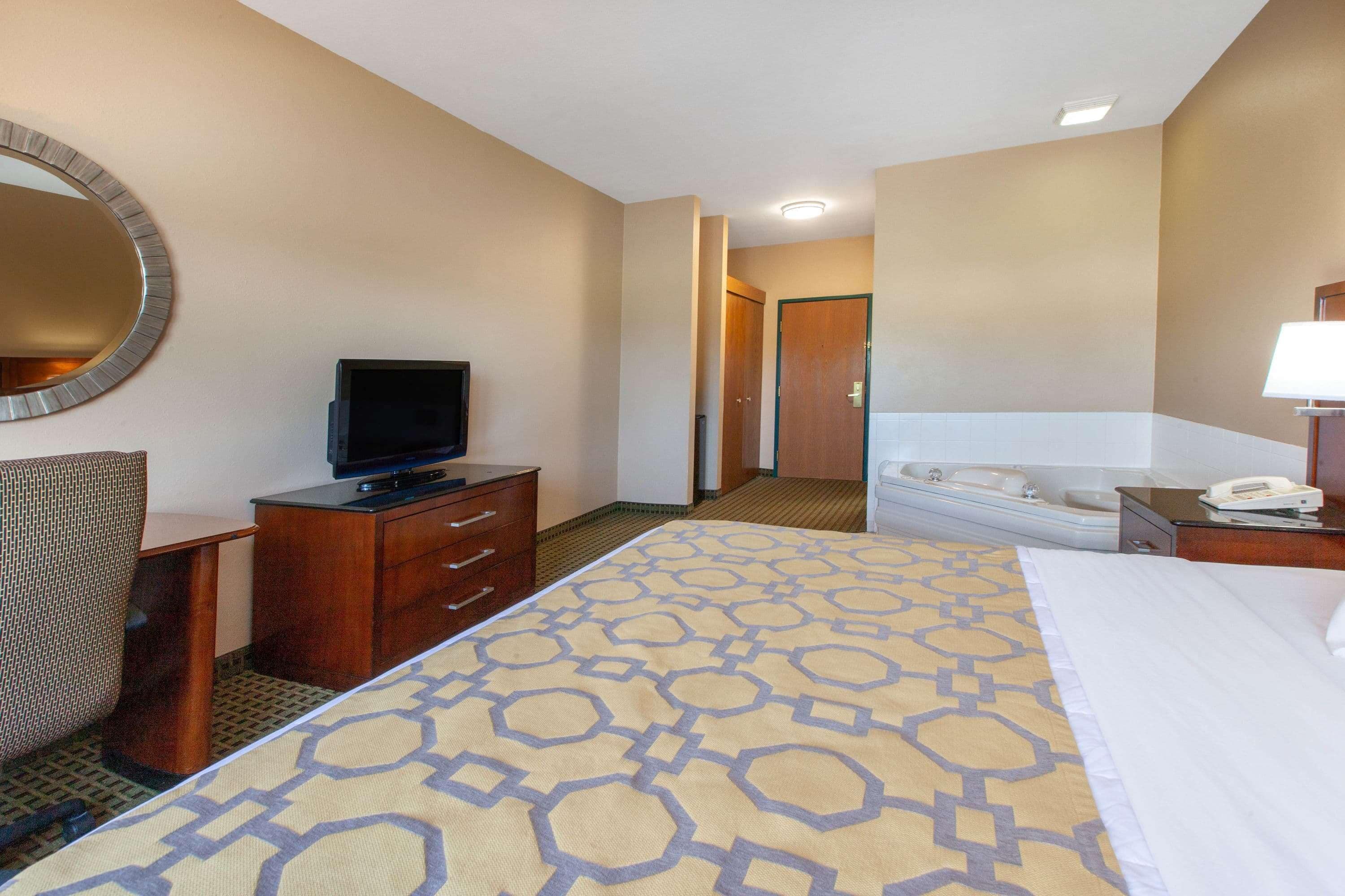 A hotel room with a bed, a television on a wooden dresser, a chair, a desk, and a bathroom with a bathtub and a toilet.
