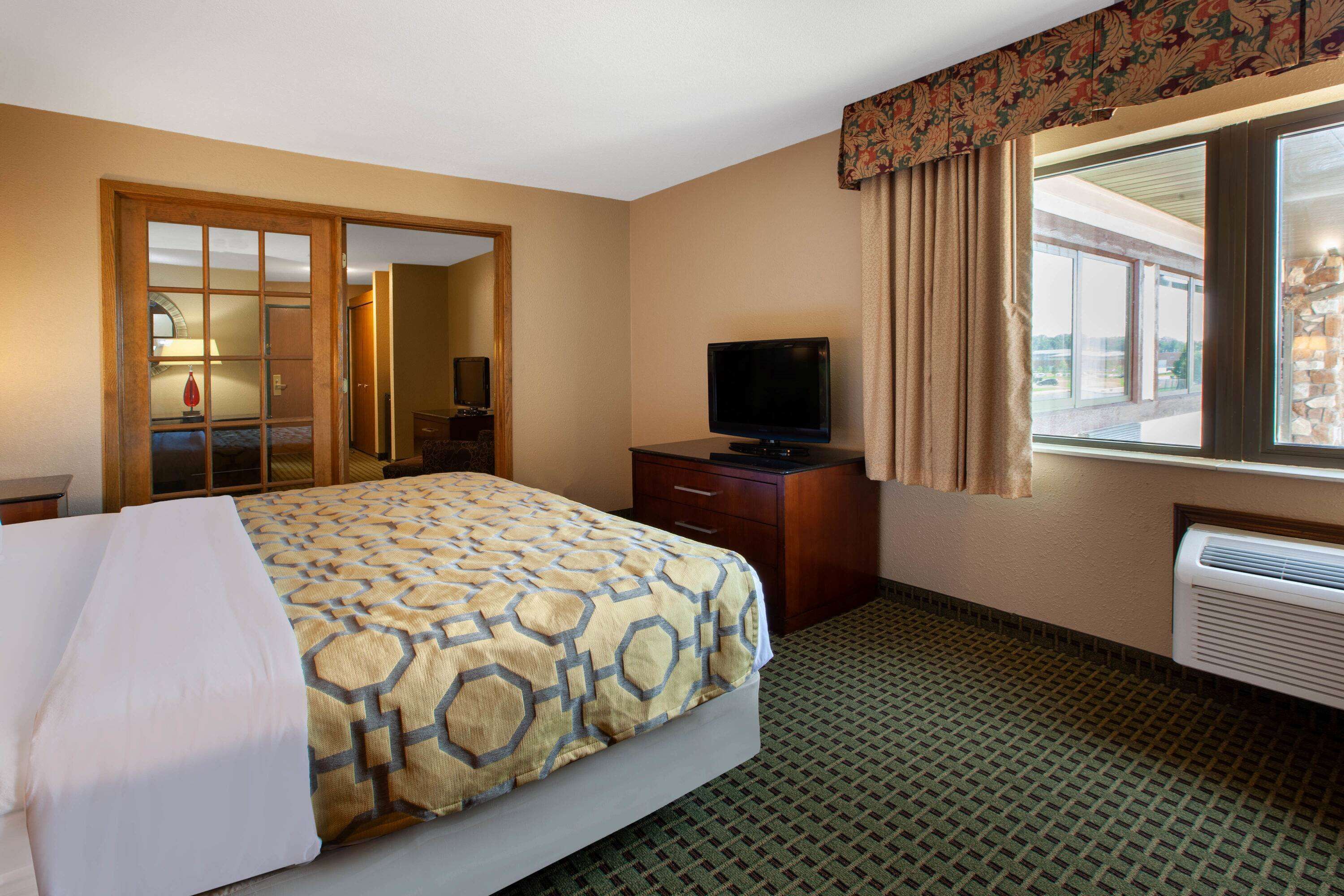 A hotel room with a bed, a television, a dresser, a mirror, and a window with curtains.