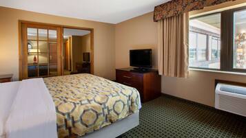 A hotel room with a bed, a television, a dresser, a mirror, and a window with curtains.