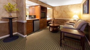 Una habitación de hotel compacta con kitchenette, comedor y sala de estar con sofá y sillón.