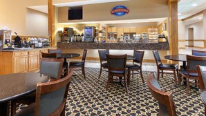 Un rincón para desayunar con sillas y mesas de madera, una barra con cafeteras, y un letrero que dice "Breakfast Corner".