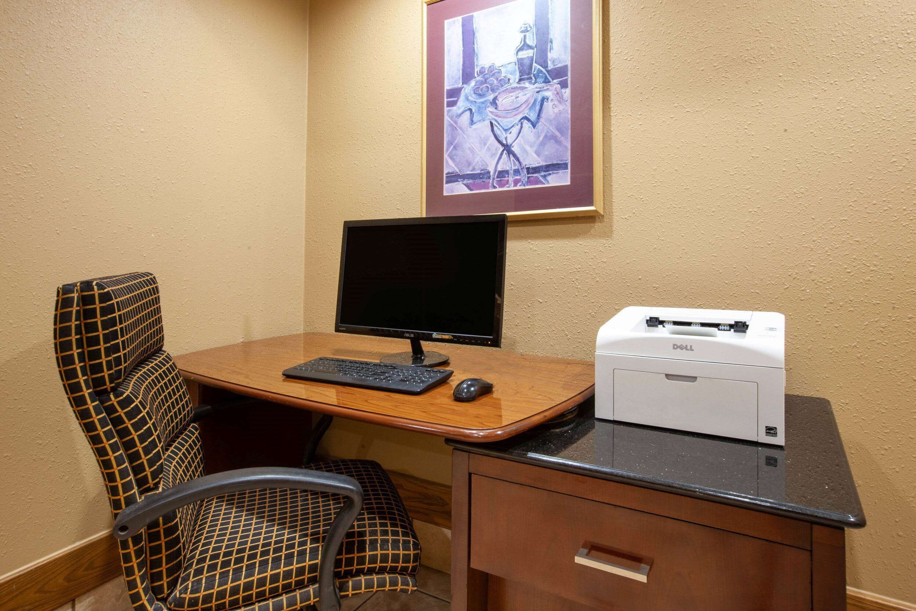 A hotel room with a wooden desk, a computer monitor, a keyboard, a mouse, and a printer.