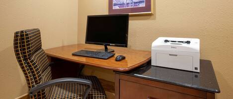 A hotel room with a wooden desk, a computer monitor, a keyboard, a mouse, and a printer.