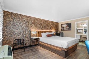 Une chambre d’hôtel moderne avec un mur décoré d’un motif en bois, un grand lit, une table de chevet, une chaise et une salle de bain visible à travers une porte ouverte.