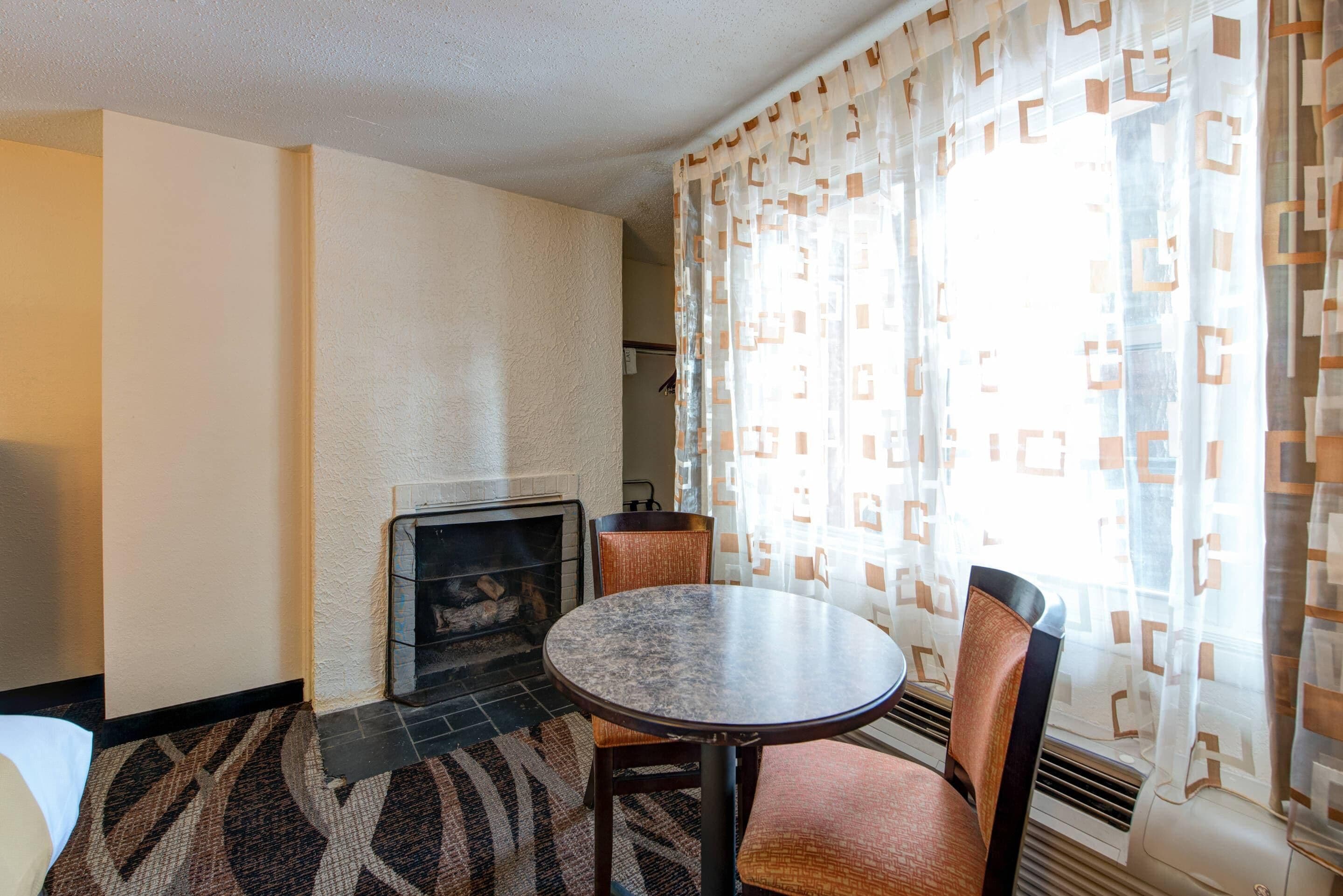 Una habitación con chimenea, una mesa redonda, dos sillas y cortinas estampadas.