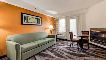 A hotel room with a green sofa, a small table with chairs, a lamp, a fireplace, and a framed picture on the wall.