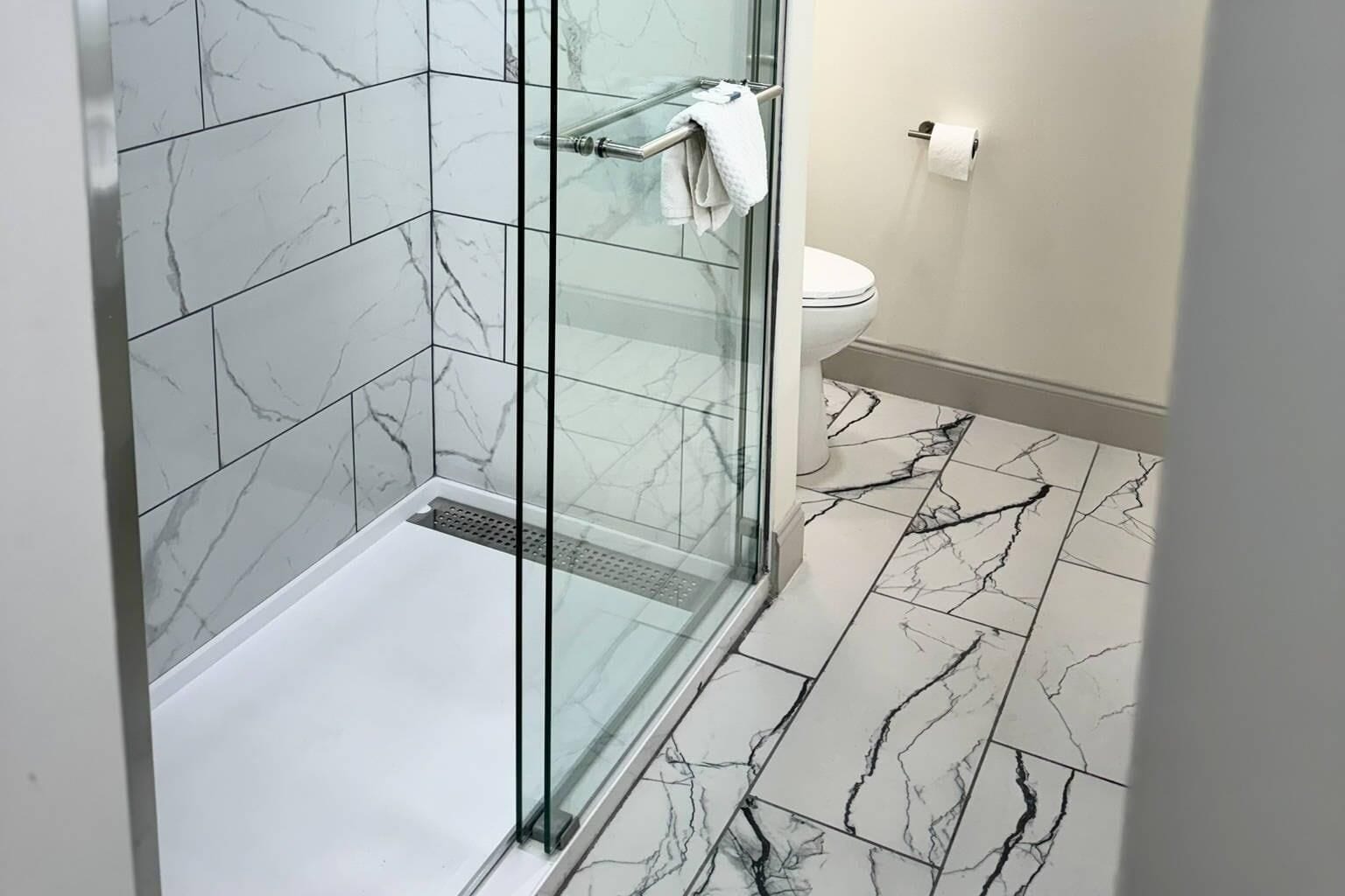 A modern bathroom with a glass-enclosed shower, a toilet, and marble-patterned flooring.
