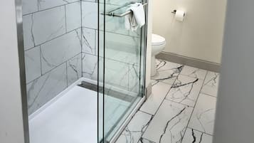 A modern bathroom with a glass-enclosed shower, a toilet, and marble-patterned flooring.
