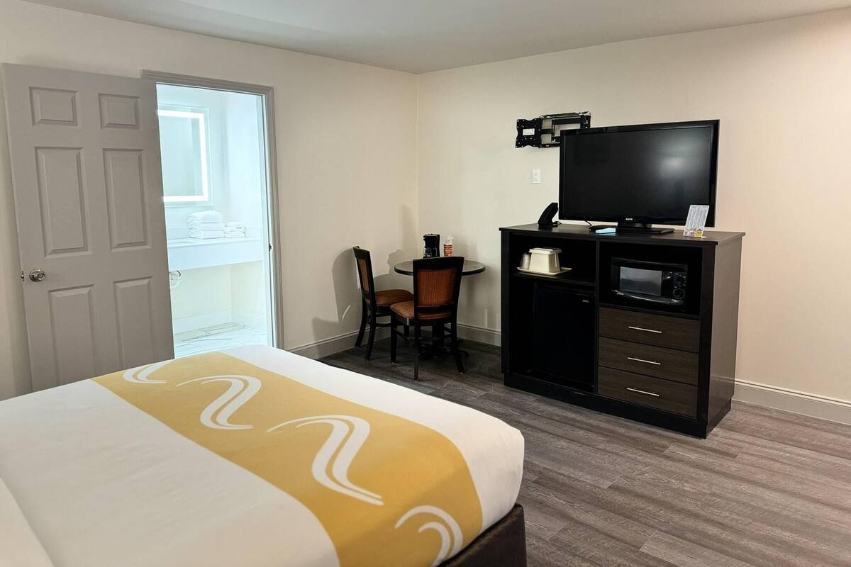 Una habitación de hotel con cama, escritorio con silla, televisor y minibar.