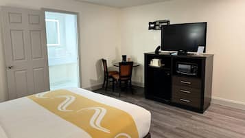 Una habitación de hotel con cama, escritorio con silla, televisor y minibar.