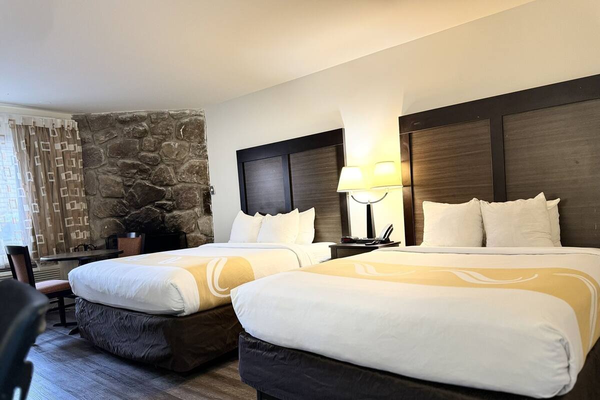 Habitación de hotel con dos camas, una pared de acento de piedra, una mesita pequeña y una silla.