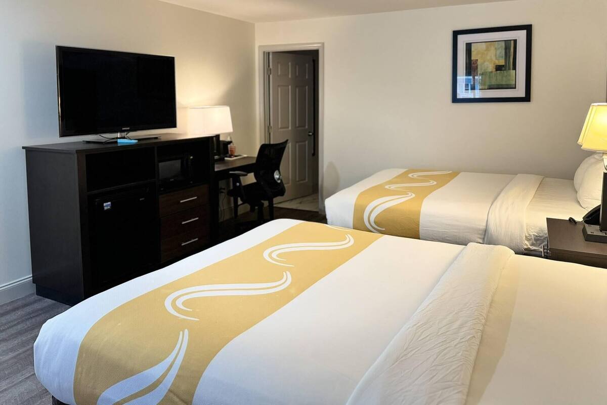 Habitación de hotel con dos camas, un escritorio con televisor, una silla y una puerta.