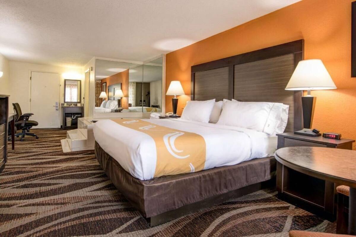 Habitación de hotel con una cama grande, un escritorio, una silla, un espejo y dos lámparas de noche.
