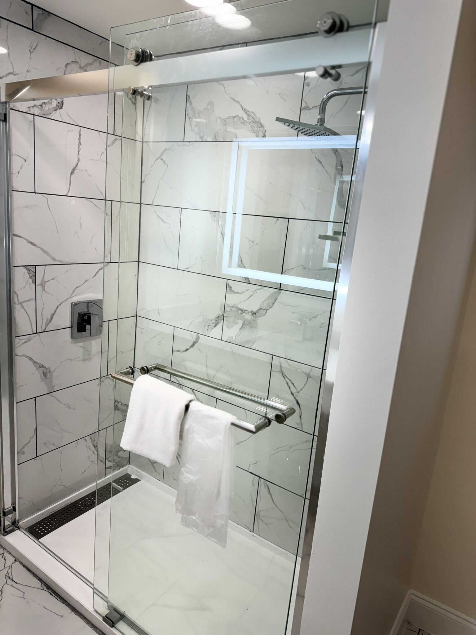 A modern bathroom with a glass-enclosed shower, marble tiles, and a glass-enclosed vanity with a towel rack.