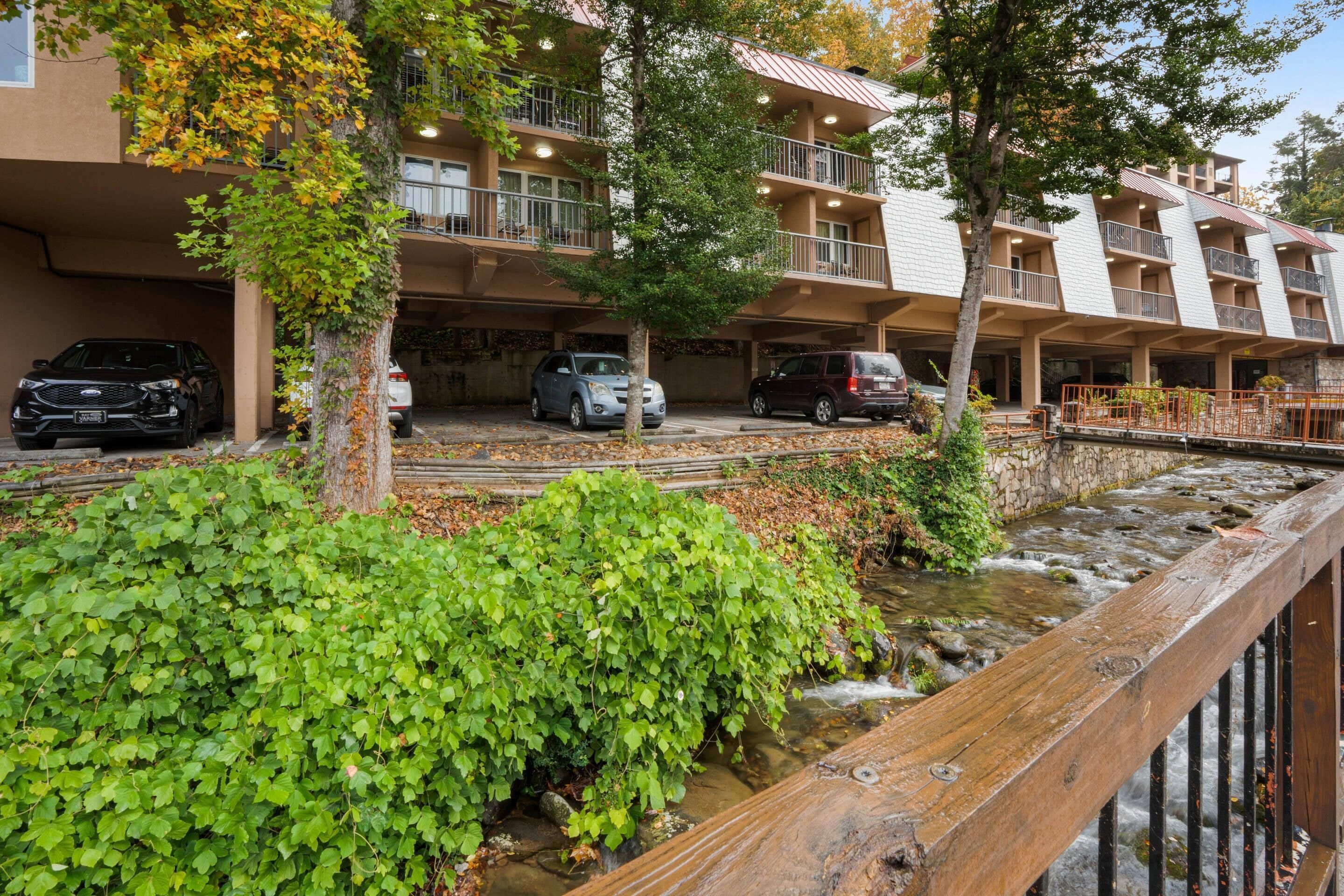 A multi-story hotel with balconies, a parking area, and a stream.