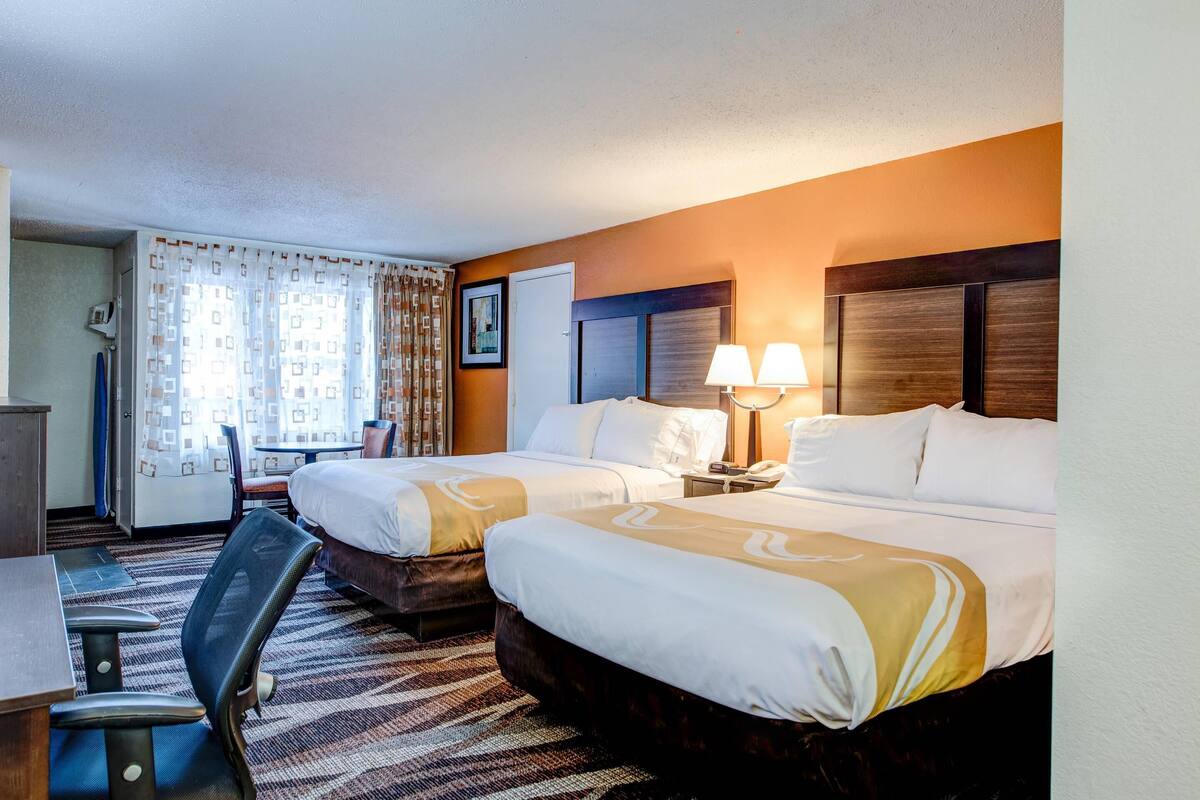 Habitación de hotel con dos camas, un escritorio, una silla y una lámpara.