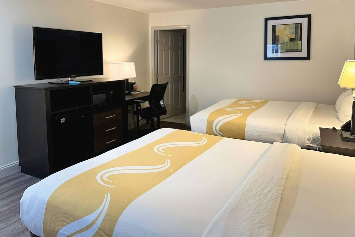 A hotel room with two beds, a desk with a TV, a chair, and a door.
