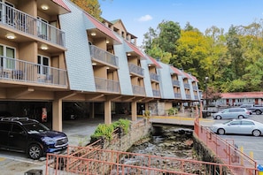 A multi-story hotel with balconies, a stone retaining wall, and a parking area.
