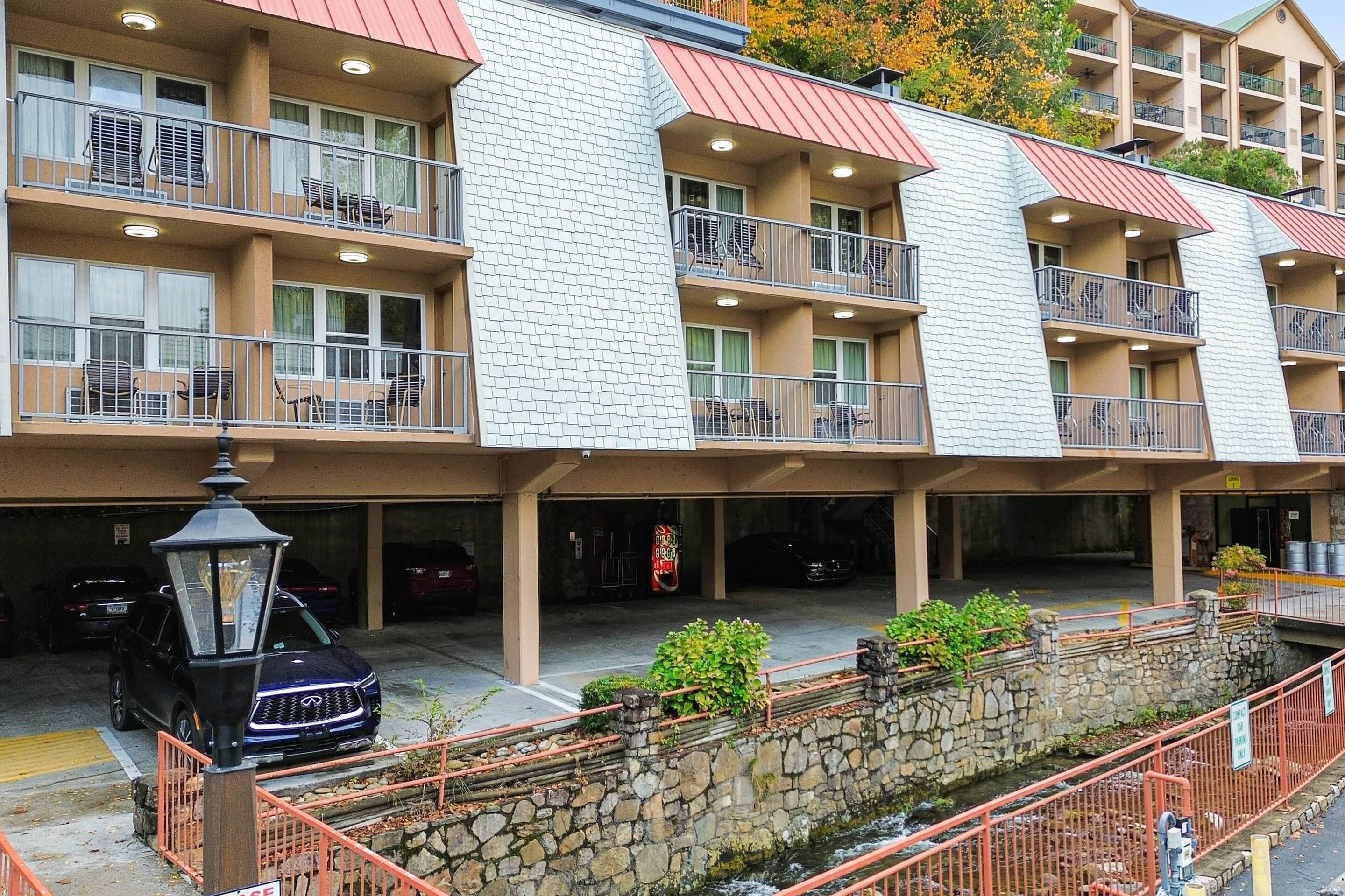 A multi-story hotel with balconies, a stone wall, and a parking area.