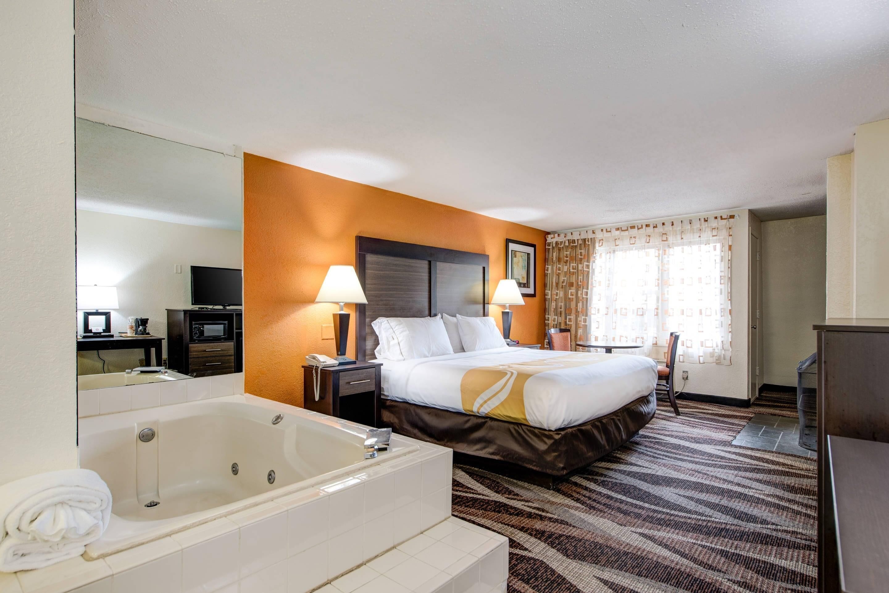 A hotel room with a large bed, a separate bathroom with a bathtub, a desk with a computer, and a television.