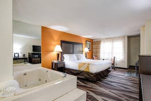 A hotel room with a large bed, a separate bathroom with a bathtub, a desk with a computer, and a television.