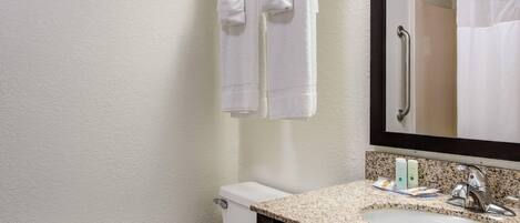Une salle de bain avec des toilettes blanches, un lavabo sur un plan de travail en granit, un miroir et un porte-serviettes avec deux serviettes.