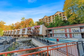 A hotel with multiple-story buildings, a swimming pool, and a rocky stream.