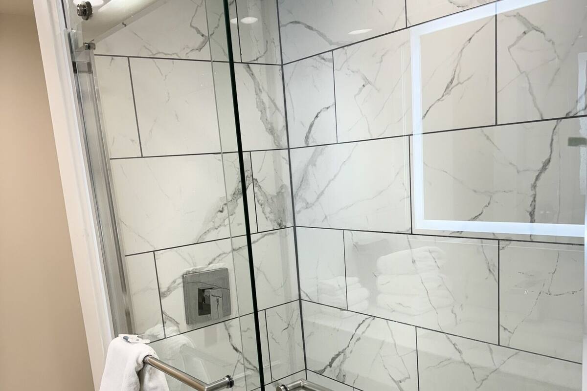 Ducha moderna con puertas de vidrio, baldosas de mármol y barra de apoyo.