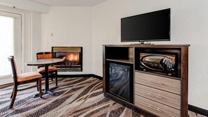 A hotel room with a fireplace, a television, a microwave, and a dining area with chairs and a table.