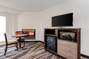 A hotel room with a fireplace, a television, a microwave, and a dining area with chairs and a table.