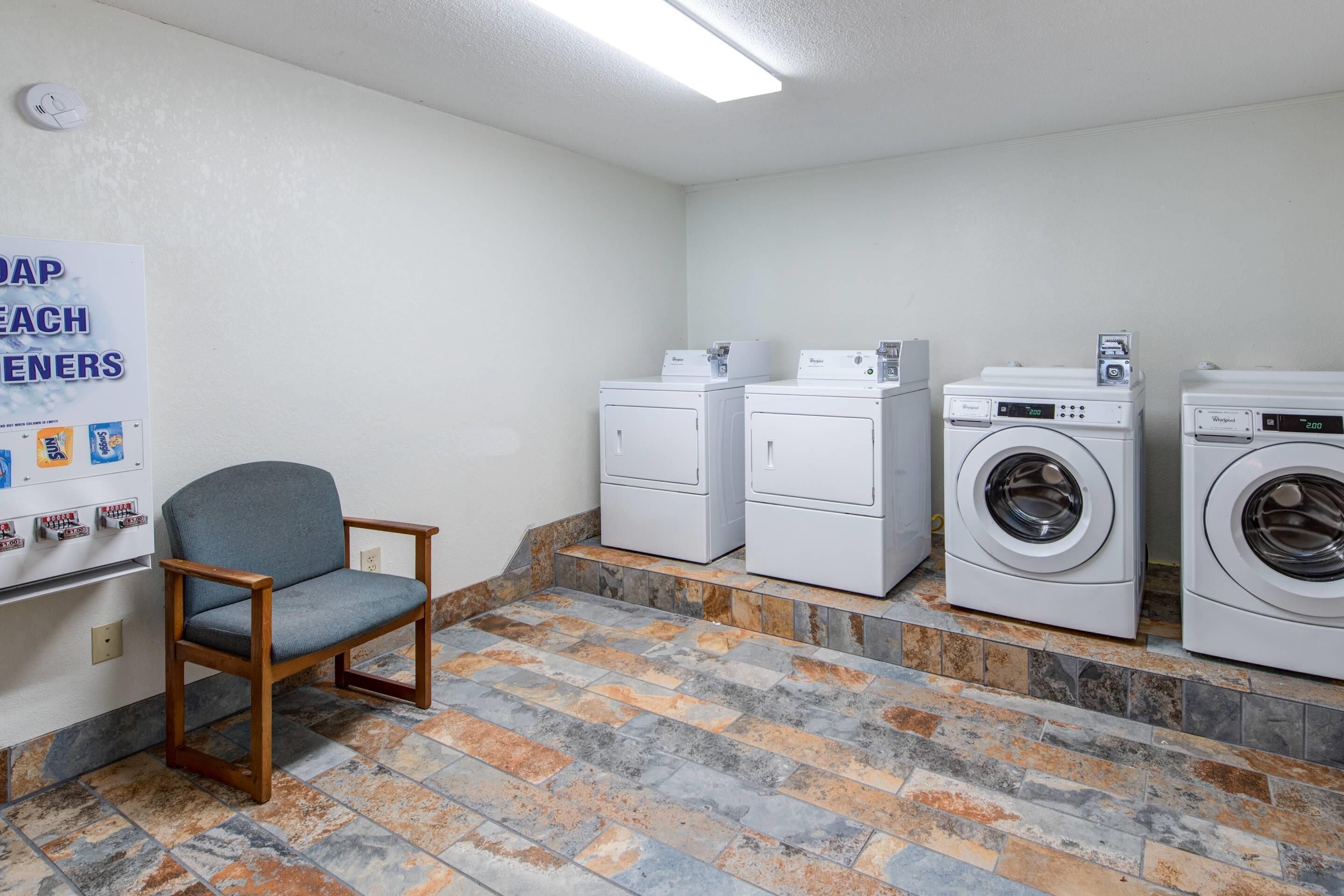 Un cuarto de lavandería con una silla, dos lavadoras apiladas y una secadora.