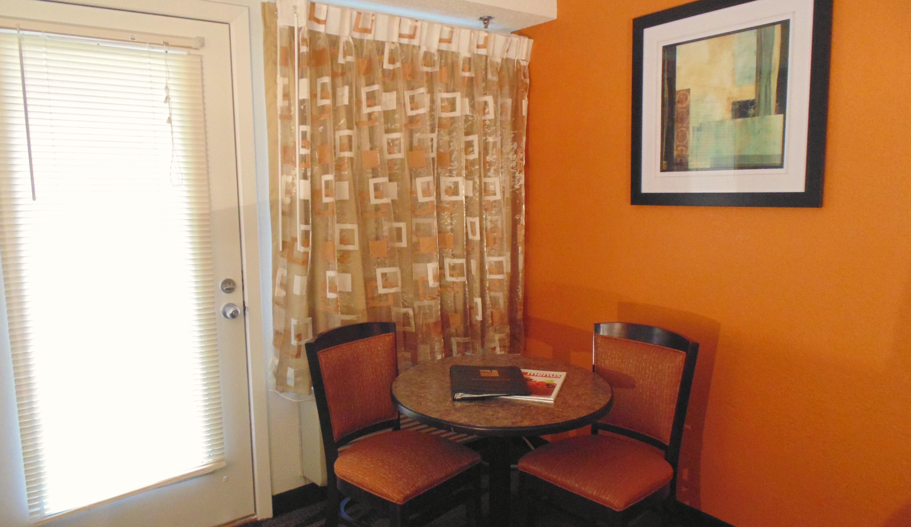 A room with a door, a patterned curtain, two chairs, a small table, and a framed picture on the wall.