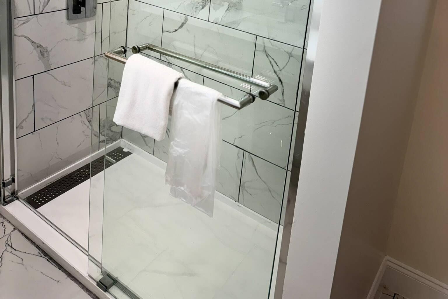 A glass-enclosed shower with a white towel on a metal towel bar.