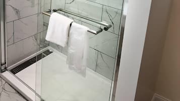 A glass-enclosed shower with a white towel on a metal towel bar.