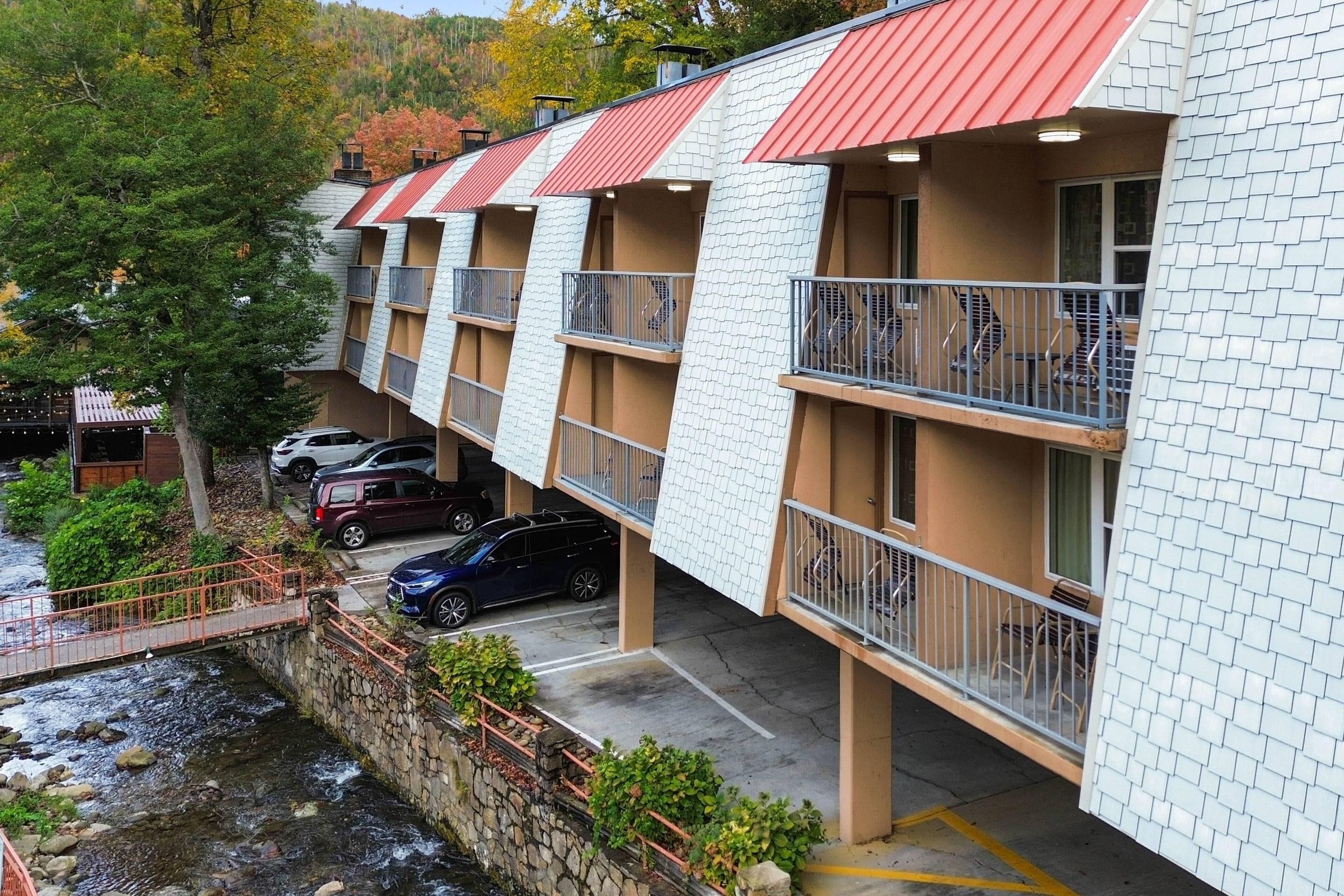 Un hotel de varios pisos con balcones, un muro de piedra de contención y un área de estacionamiento.